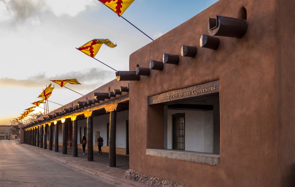 Adobe-style historic building lined with colorful flags, captured at dusk.