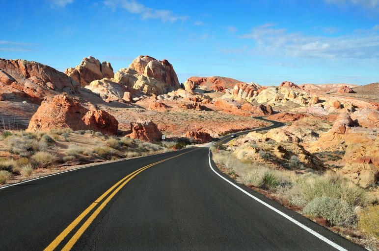 A view of a winding road surrounded by colorful rocky hills and desert landscape under a clear blue sky.