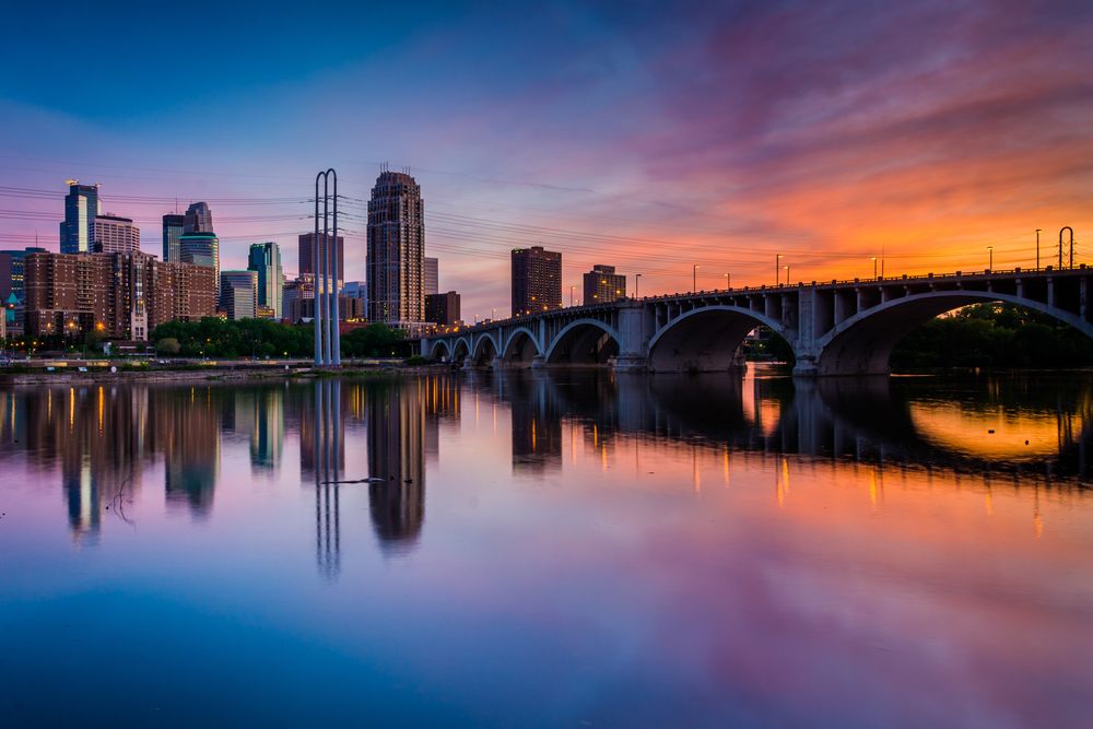 Cityscape reflecting on a calm river during a colorful sunset.