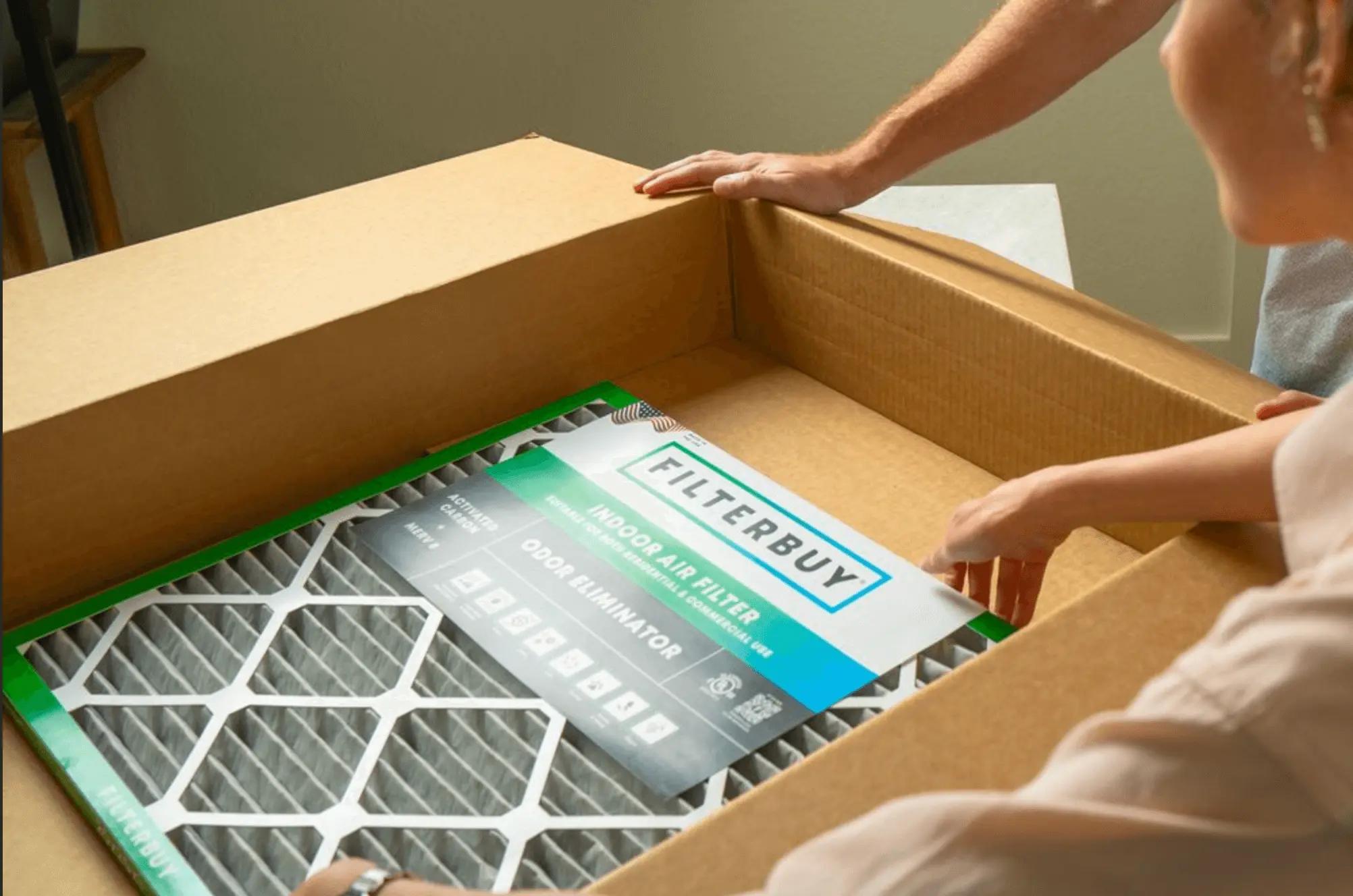 An image of two people opening a Filterbuy indoor air filter box, showing a close-up of the odor eliminator air filter inside.