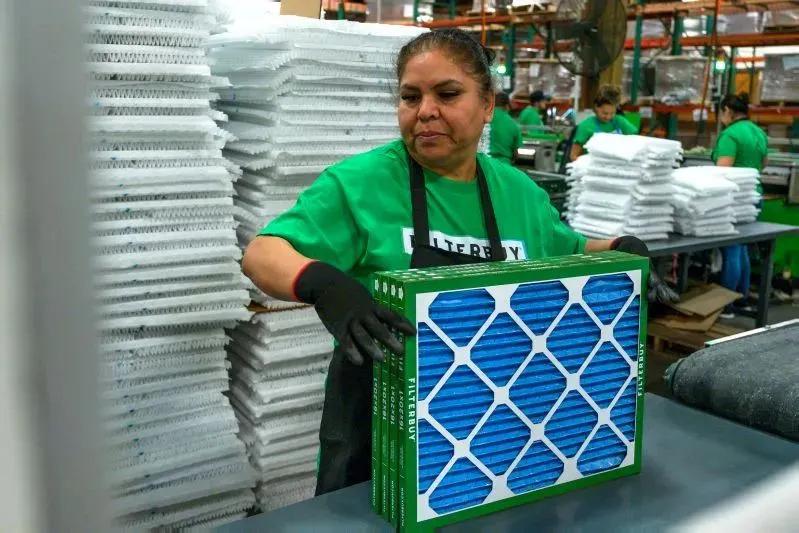 A view of a Filterbuy factory worker handling a blue air filter on the production floor.