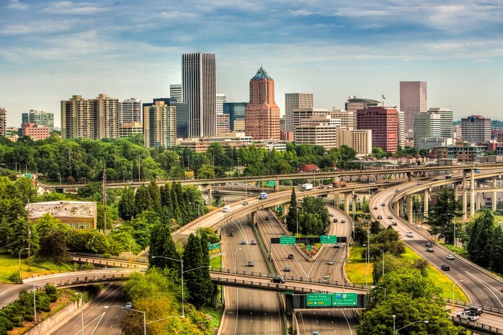 View of Portland skyline featuring tall buildings and complex highway system surrounded by greenery.