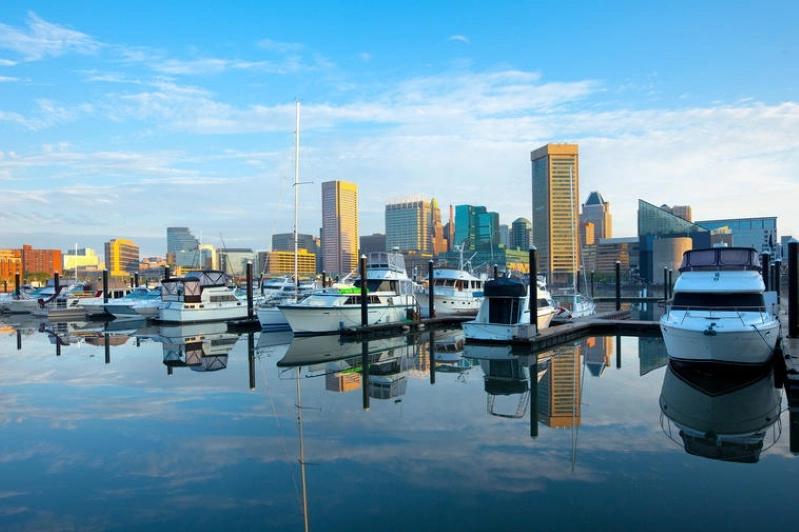 Cities Where Remote Workers Log the Most Hours - Images of the Baltimore Harbor with boats docked and the city skyline reflecting on the water, capturing a peaceful morning scene in the city.