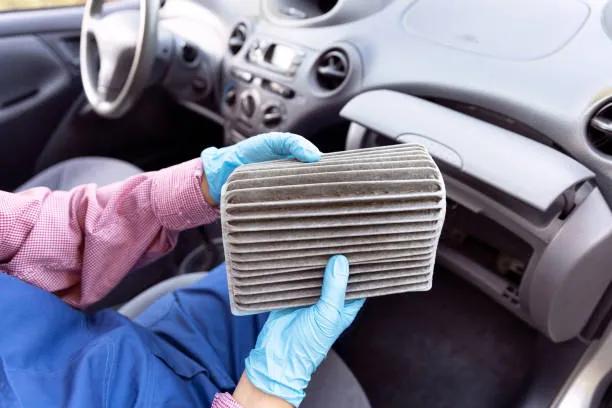 A view of a mechanic holding a used car air filter inside a vehicle, highlighting the need for the best car and engine air cleaner filter replacements online.