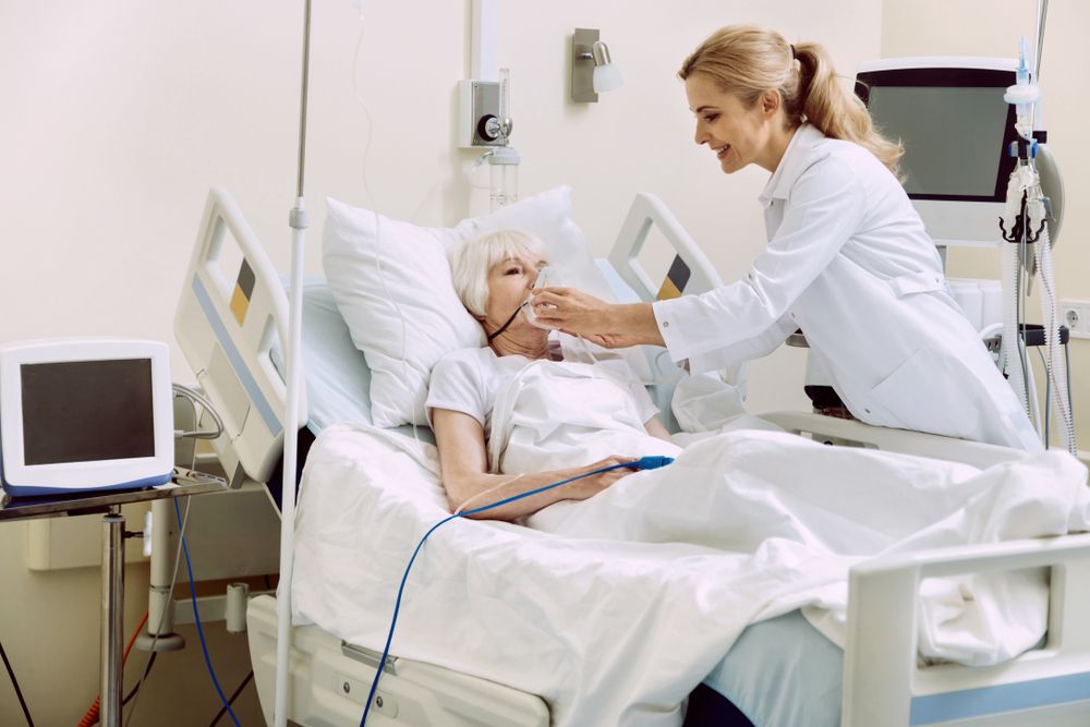 Nurse assisting an elderly female patient in a hospital bed by offering her an oxygen mask.