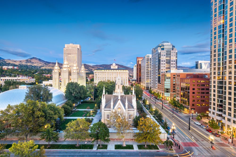 Tree-lined boulevard leading through a city surrounded by mountains and high-rise buildings.