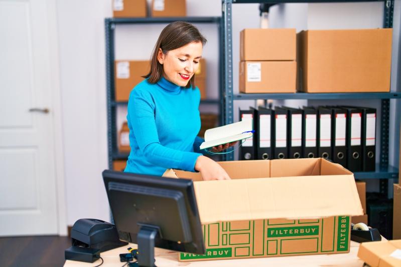 Skuttle Humidifier Air Filter Replacement Guide - Image of a woman unpacking a Filterbuy box in an office setting, preparing air filters for use while smiling and reviewing a notebook.
