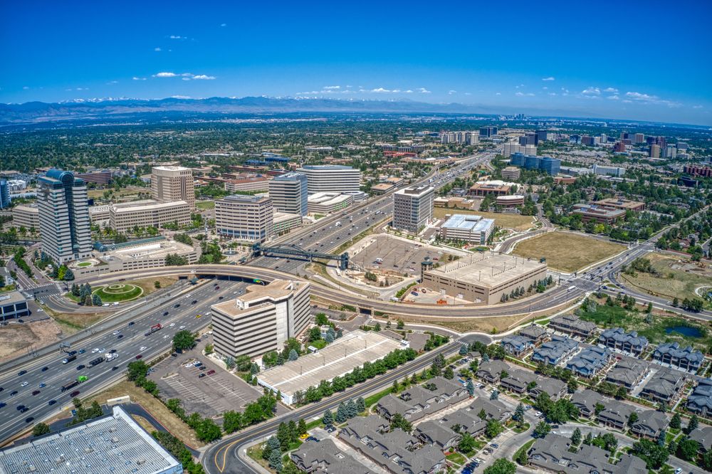 A wide shot of modern office buildings and highways surrounded by greenery with mountains in the background.