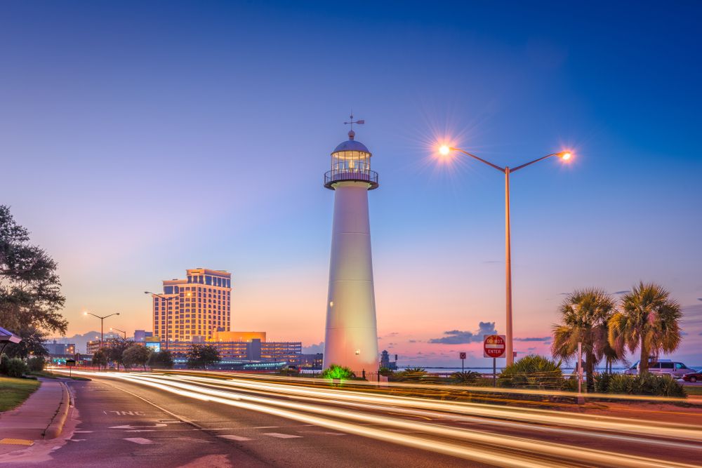 Lighthouse illuminated by streetlights with motion blur from passing cars.