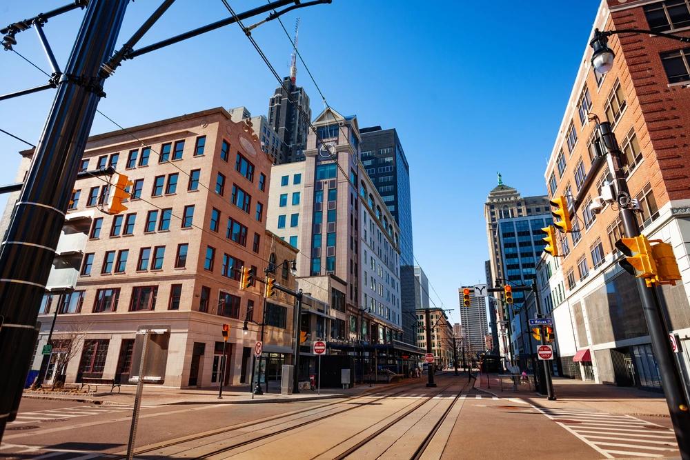 Image of downtown Buffalo, New York featuring historic buildings, modern offices, and light rail tracks under a clear blue sky.