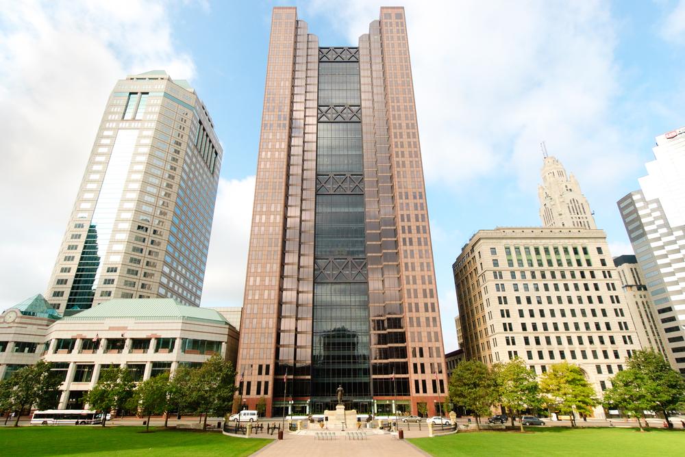 Downtown Columbus, Ohio featuring modern high-rises and historic architecture under a bright sky with green lawn in the foreground.