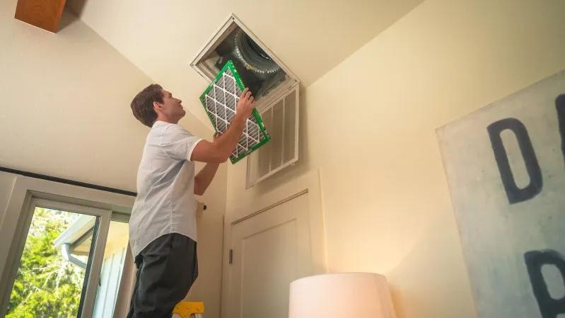 View of a man installing a Filterbuy 18x30x2 air filter into a ceiling vent for improved HVAC performance and indoor air quality.