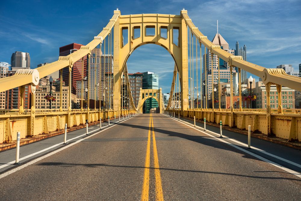 Daytime view of the iconic yellow bridge in Pittsburgh with city buildings in the distance.