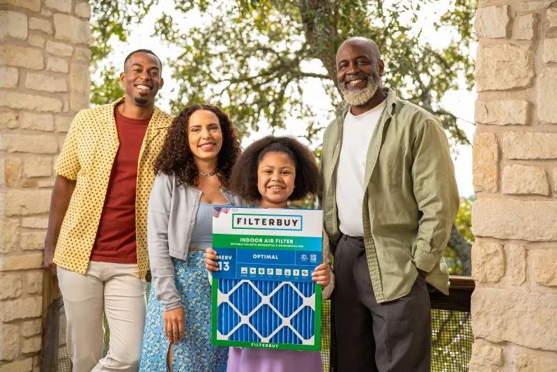 Smiling family holding a Filterbuy air filter outdoors, ready for installation to improve air conditioner efficiency.