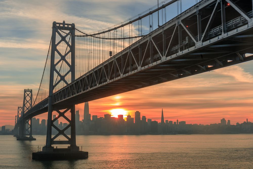 Bay Bridge and San Francisco skyline at sunrise with orange and pink skies