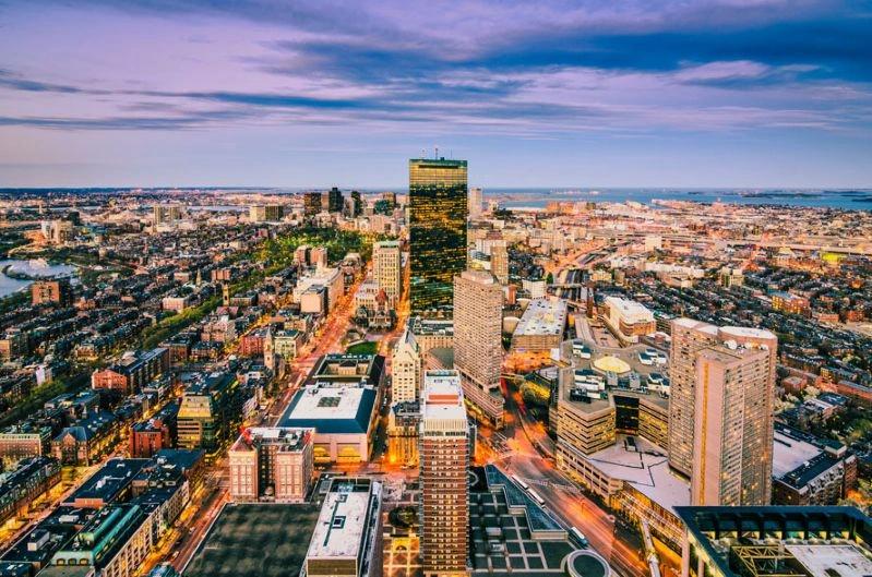 Cities with the Most Asthma Cases - Image of Boston's city skyline, showcasing tall buildings with traffic moving on highways, and a colorful sky in the background.