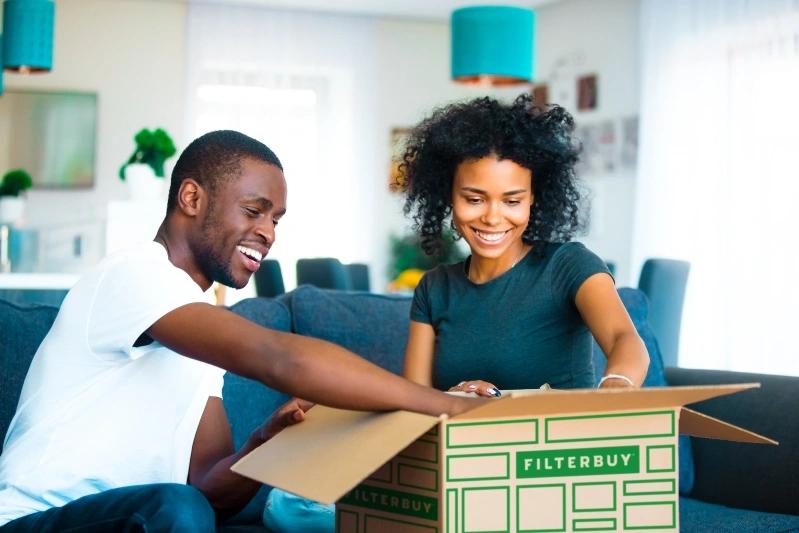 The Ultimate Guide to Choosing the Right Air Conditioner Filter Cover for Your Home - Image of a woman and man smiling while unpacking Filterbuy air filters from a box in their home.