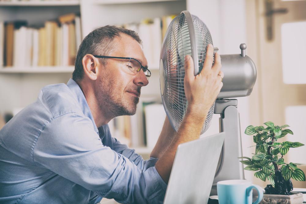 Image of a man grabbing the sides of an electric fan just to cool down his body due to the intense heat.