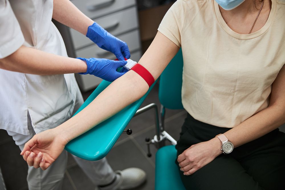 Healthcare worker in gloves applying a tourniquet on a woman's arm in a medical clinic.