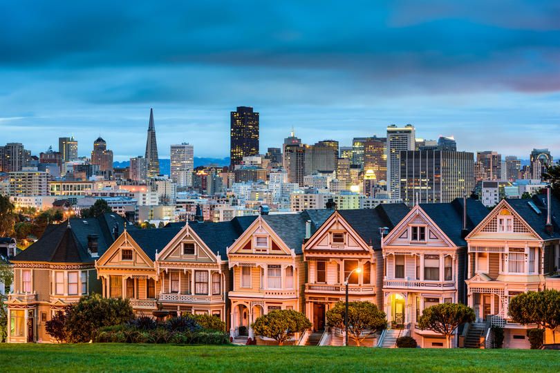Victorian-style row houses in front of a modern skyline during twilight