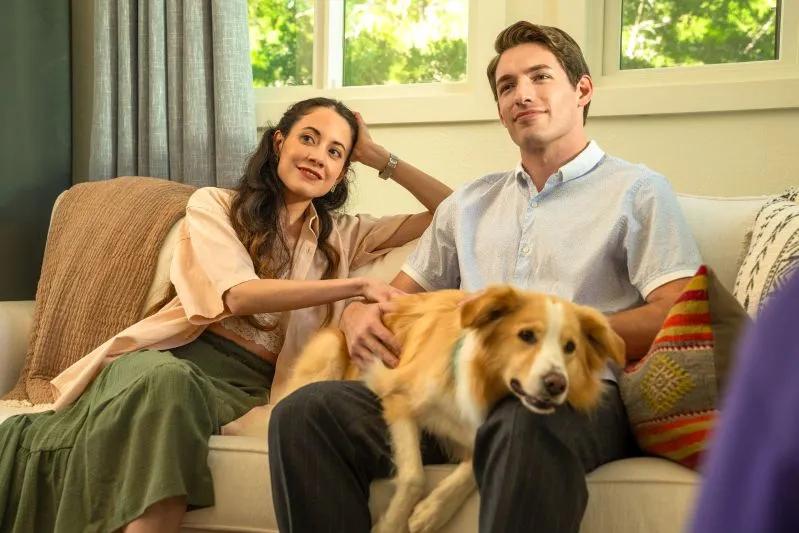View of a couple sitting on couch with happy dog in cozy living room with natural light.