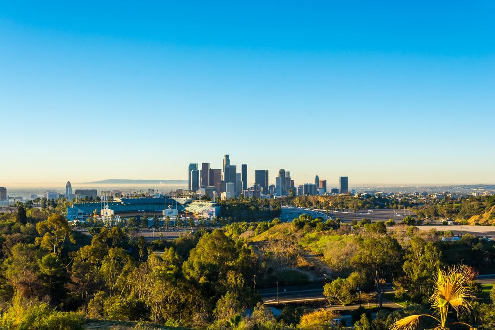 Downtown Los Angeles skyline with Dodger Stadium and tree-covered hills in the foreground.
