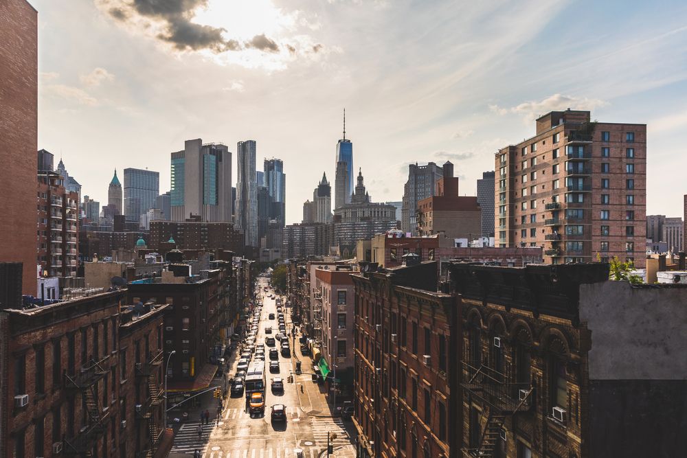 Urban skyline with a street lined by mid-rise buildings and heavy traffic at sunset.
