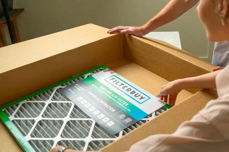 A view of a person unboxing Filterbuy 15.5x29x1 air filters from a large cardboard package, showcasing quality HVAC filter delivery.