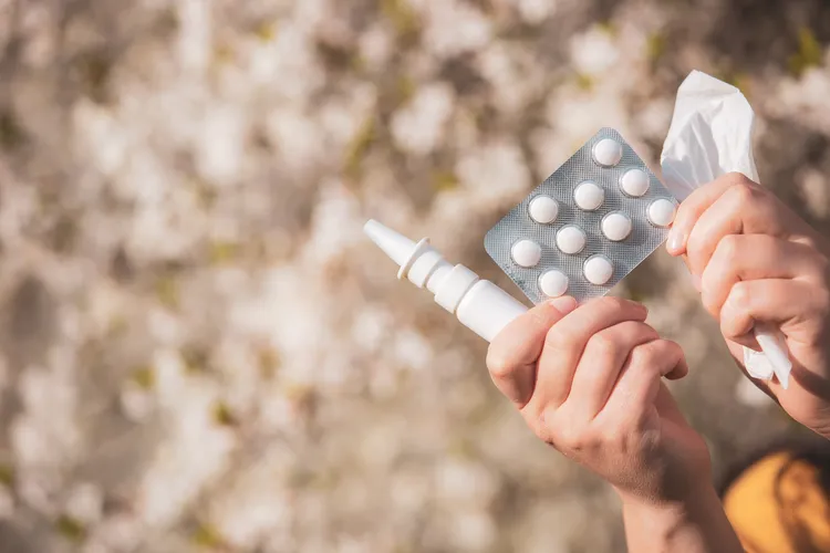 View of a person holding allergy relief medications, including nasal spray, tablets, and tissues