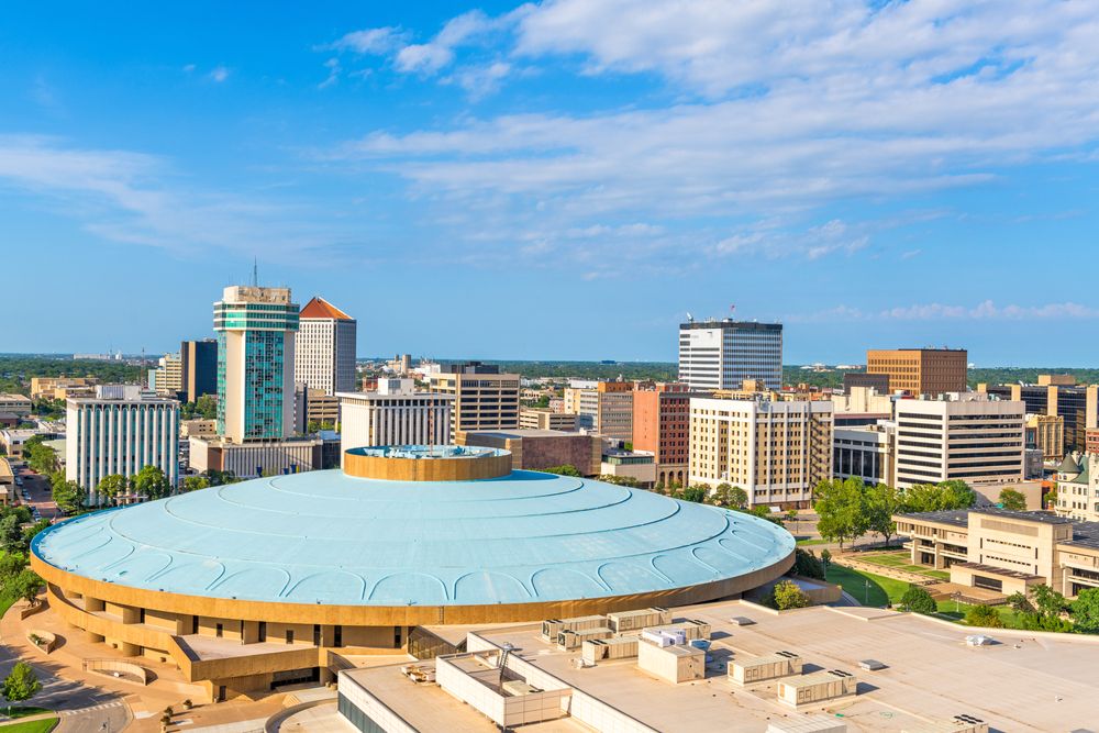 Cityscape featuring a large round domed building surrounded by modern and mid-rise buildings on a sunny day.