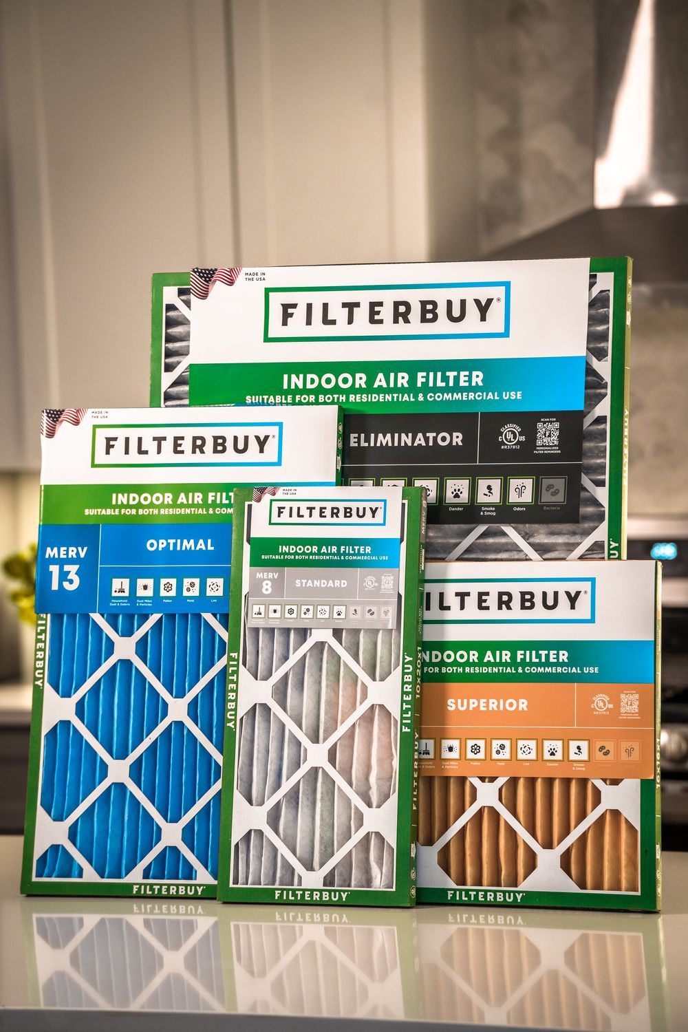 An image of 20x20x5 Filterbuy air filters in multiple colors (gray, blue, yellow, and white) neatly displayed on a kitchen counter.