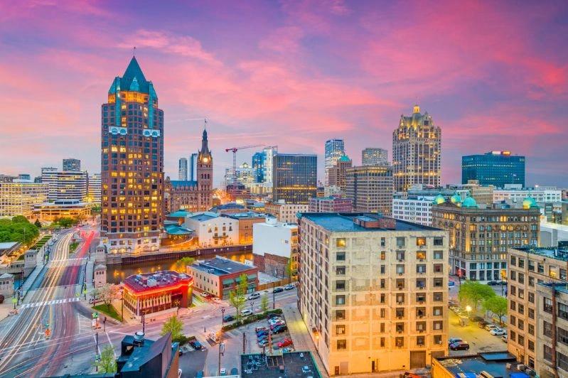 Cities with the Most Asthma Cases - Image of Milwaukee city skyline at sunrise, showcasing tall buildings with traffic moving on highways, and a colorful sky in the background.