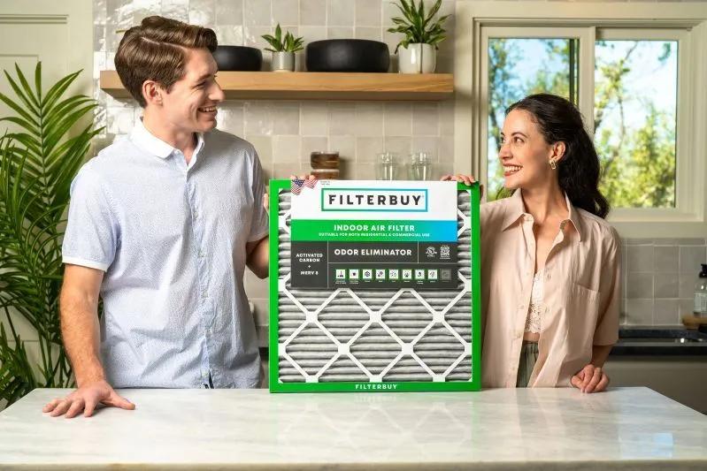 A view of a smiling man and woman holding a Filterbuy air filter in a modern kitchen.