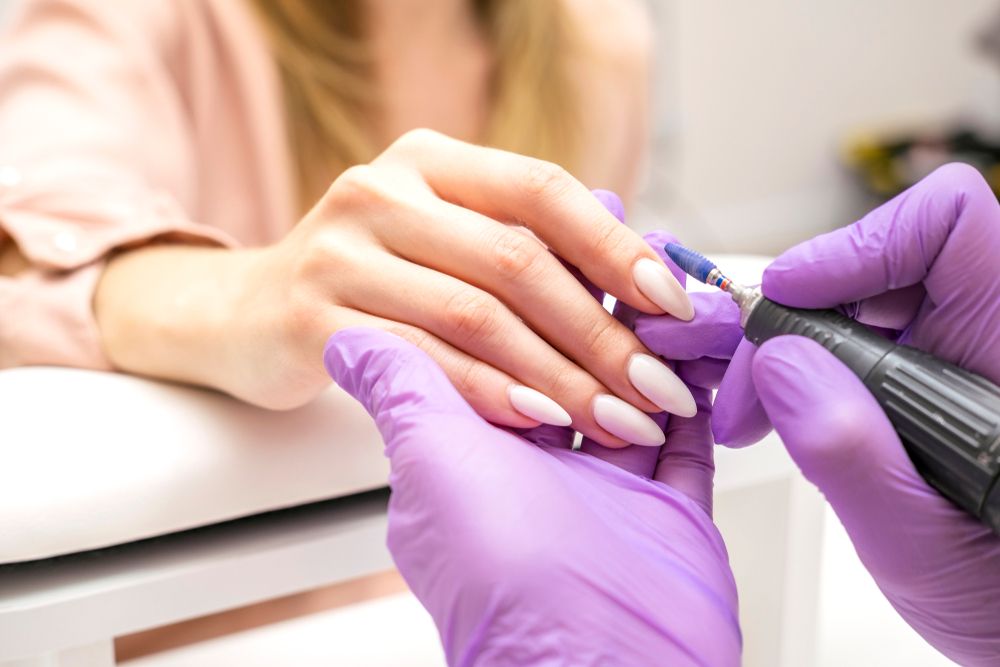 Nail technician wearing purple gloves performing manicure with electric file