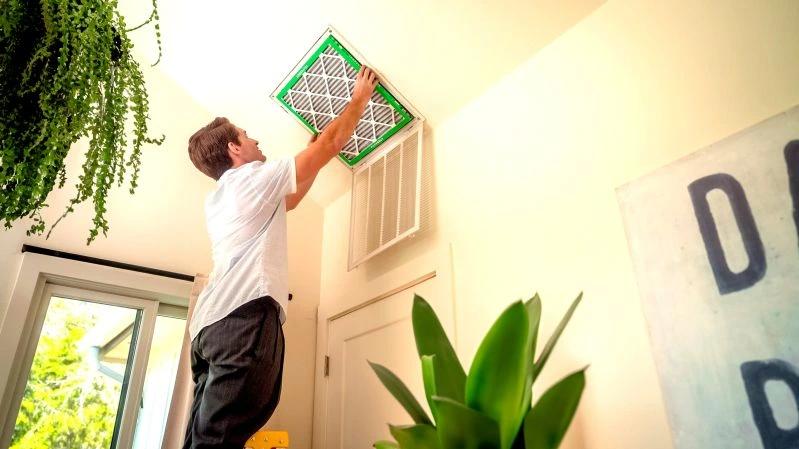 View of - A man installing a new air filter into a ceiling vent, ensuring clean indoor air with a high-quality Filterbuy HVAC filter.