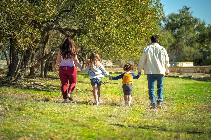 Enhance Your Home’s Air Quality with Scented HVAC Air Filters - Image of a family of four walking hand-in-hand through a grassy field under the trees, enjoying a sunny day outdoors.