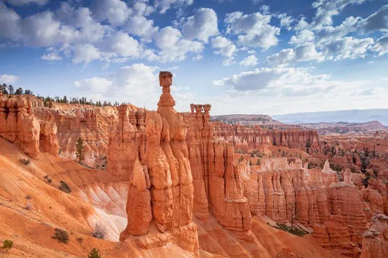 View of towering red rock hoodoos under a partly cloudy sky in a scenic desert canyon landscape.