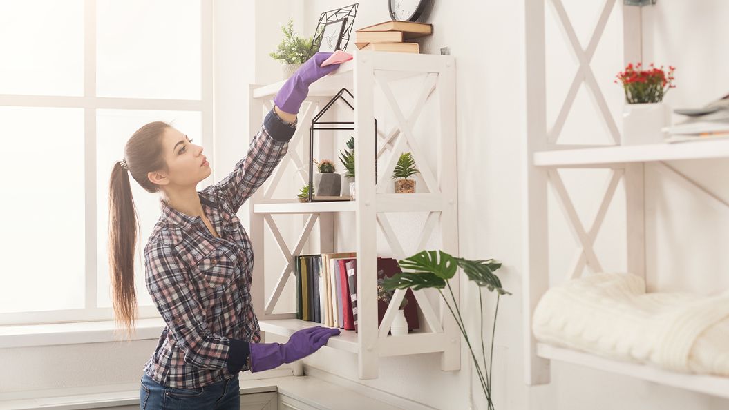 Woman cleaning shelves and dusting in a bright room