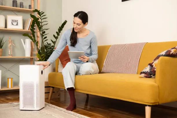 A view of a woman adjusting a HEPA air purifier in a cozy living room.