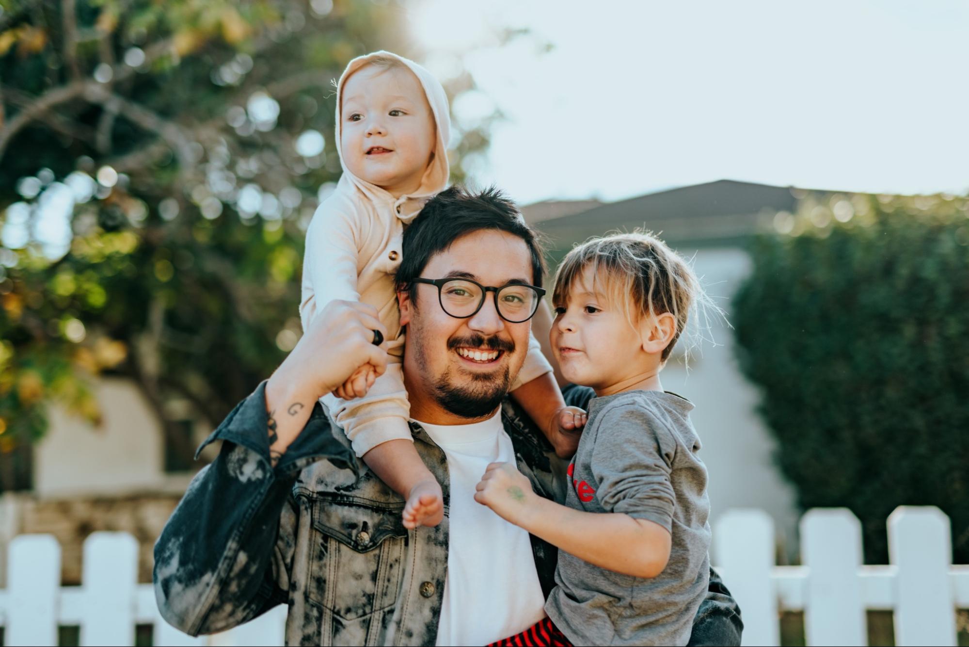 Father smiling and holding two young children outdoors