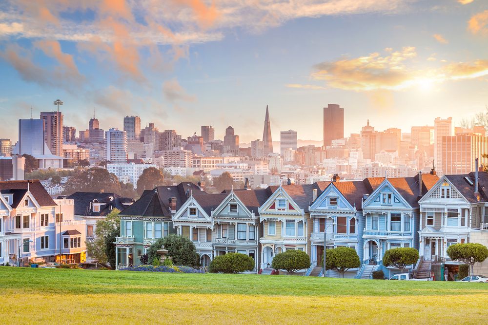 A view of San Francisco's skyline at sunset, with the iconic painted ladies houses in the foreground and the cityscape in the background, bathed in warm golden light.