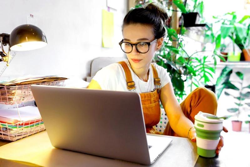 view of - A young woman works comfortably on her laptop in a bright, plant-filled room