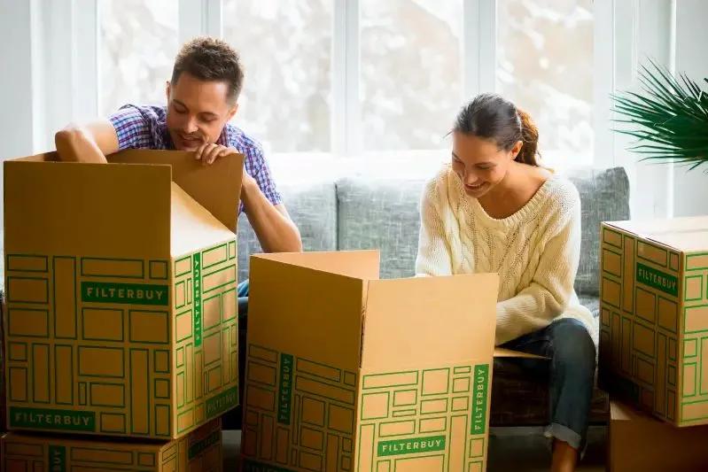 A view of a smiling couple unpacking Filterbuy boxes in a bright living room, suggesting a new home or air filter delivery experience.