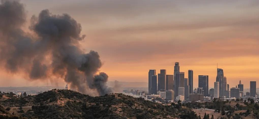 View of live wildfire and smoke conditions over Los Angeles, CA, showing active fire smoke plumes near the city skyline at sunset, supporting a real-time wildfire and air quality tracking map for Southern California.