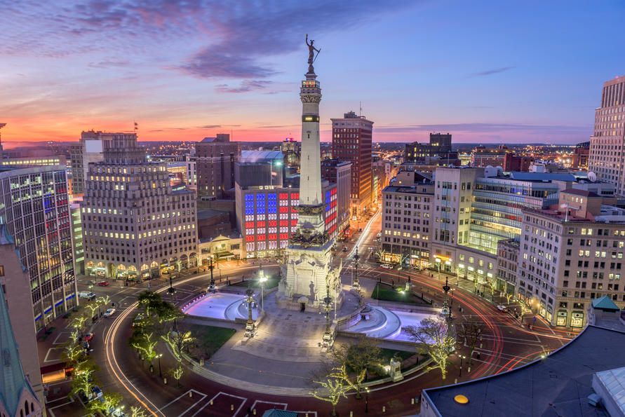 Central monument surrounded by circular plaza and city buildings at dusk