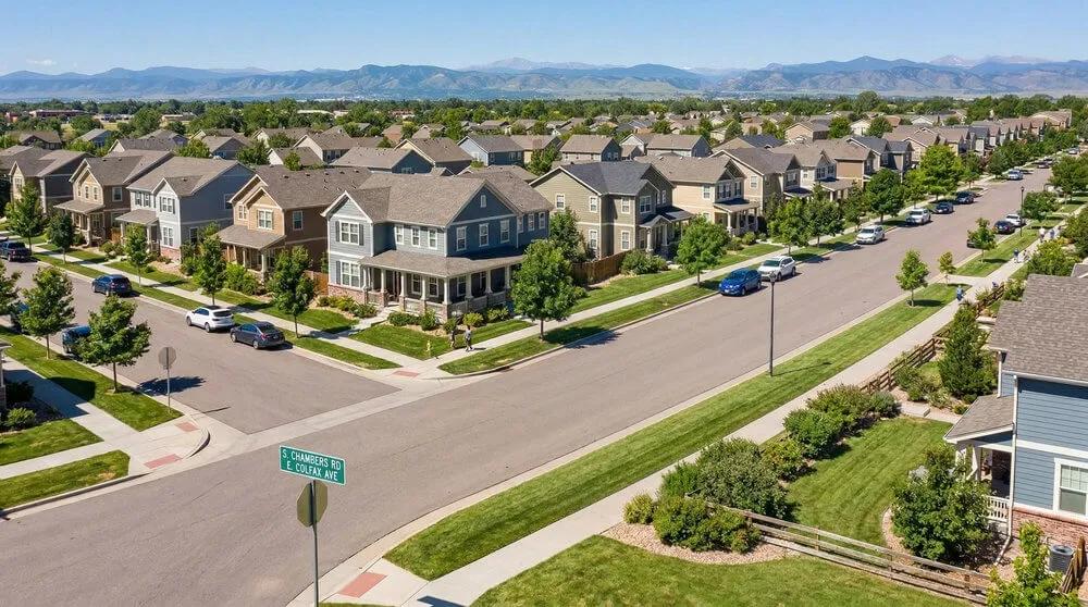 An image of a sunny suburban neighborhood in Aurora, Colorado, featuring well-kept houses, tree-lined streets, and distant mountains.