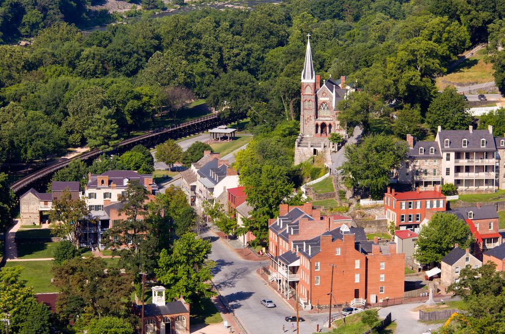 Elevated view of a quaint historic town with brick buildings, a stone church on a hill, and surrounding green forest.