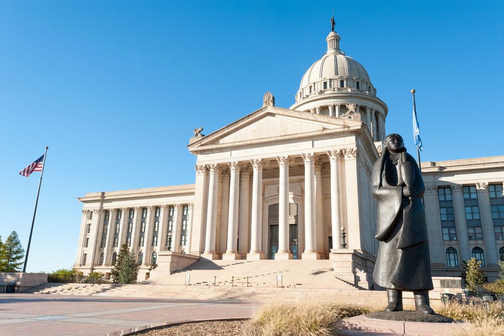 Large domed government building with a statue in front, bathed in bright daylight.