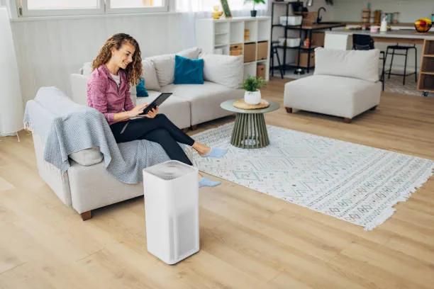 A view of a woman relaxing in a living room with an air purifier, highlighting when and how often to change a HEPA air filter for clean air.