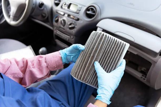 A view of a mechanic holding a used cabin AC air filter inside a car with the glove compartment removed, showing the filter's location